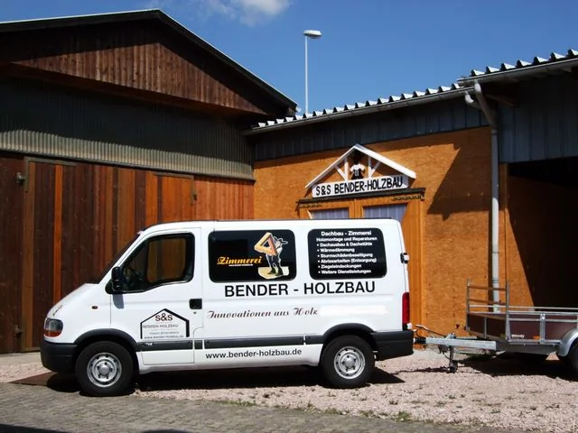 Weißer Kastenwagen mit Anhänger von S&S Bender-Holzbau vor der Werkstatt mit Schriftzug Innovationen aus Holz.